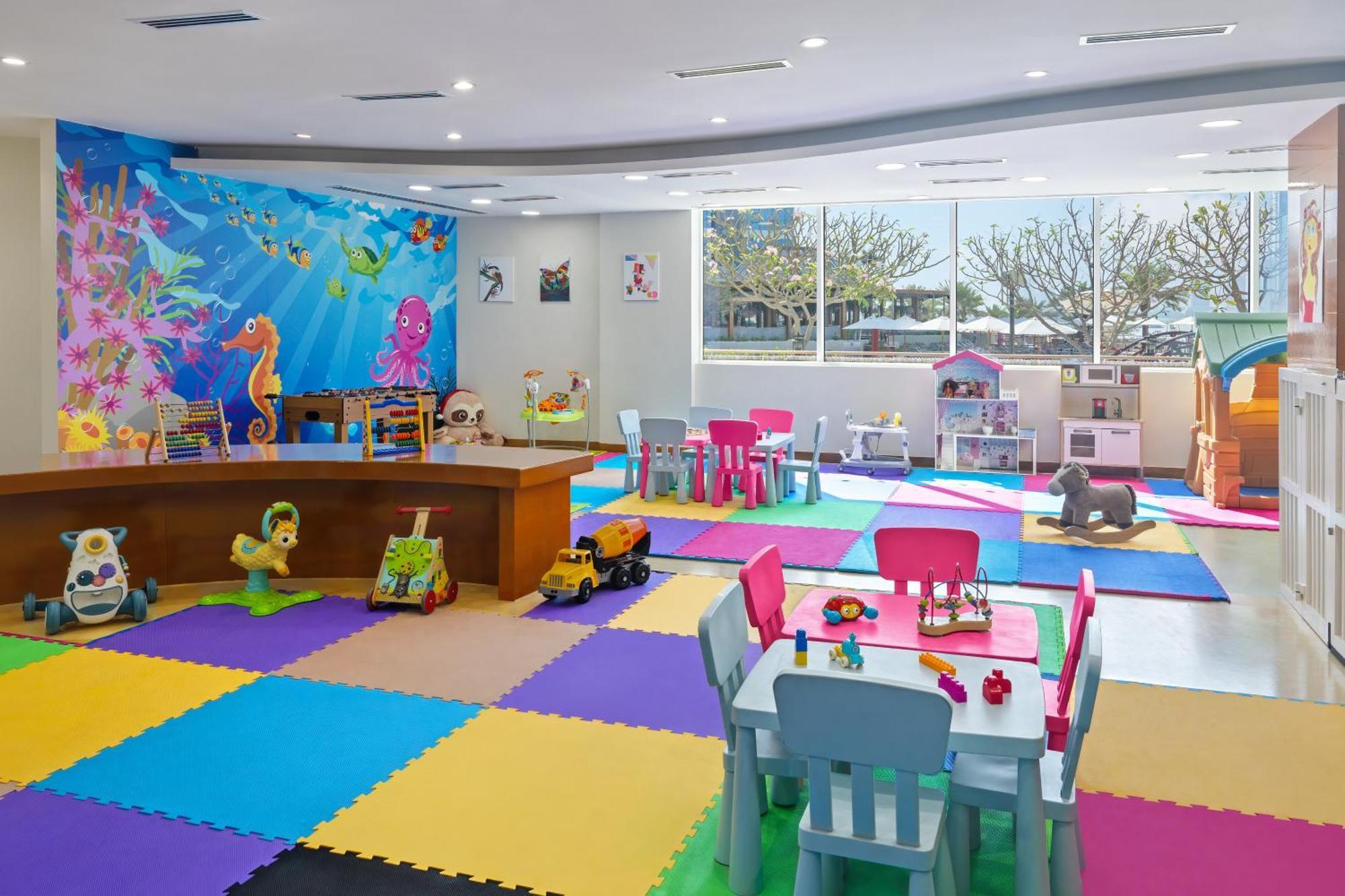 דובאי Dukes The Palm, A Royal Hideaway Hotel מראה חיצוני תמונה The photo shows a bright and colorful children's playroom. The floor is covered with interlocking foam mats in various colors, including blue, green, yellow, and purple. There is a large table made of wood at the center, surrounded by colorful chairs
